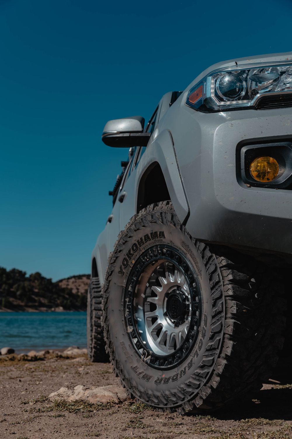 Close-up view of an off-road truck wheel with rugged all-terrain tires against a blue sky background.
