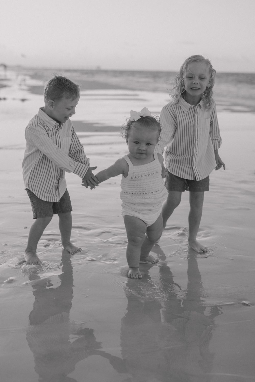 Three children in matching striped shirts play together at the beach during sunset.