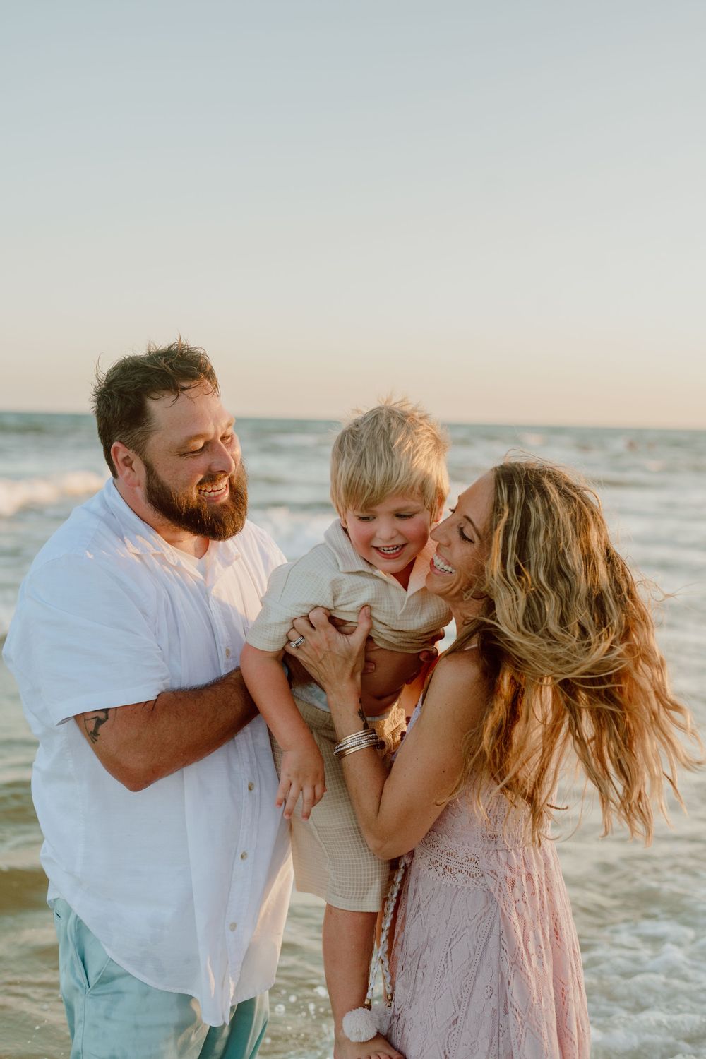 A family shares joyful moments and embraces while playing together on a sunny beach at sunset.