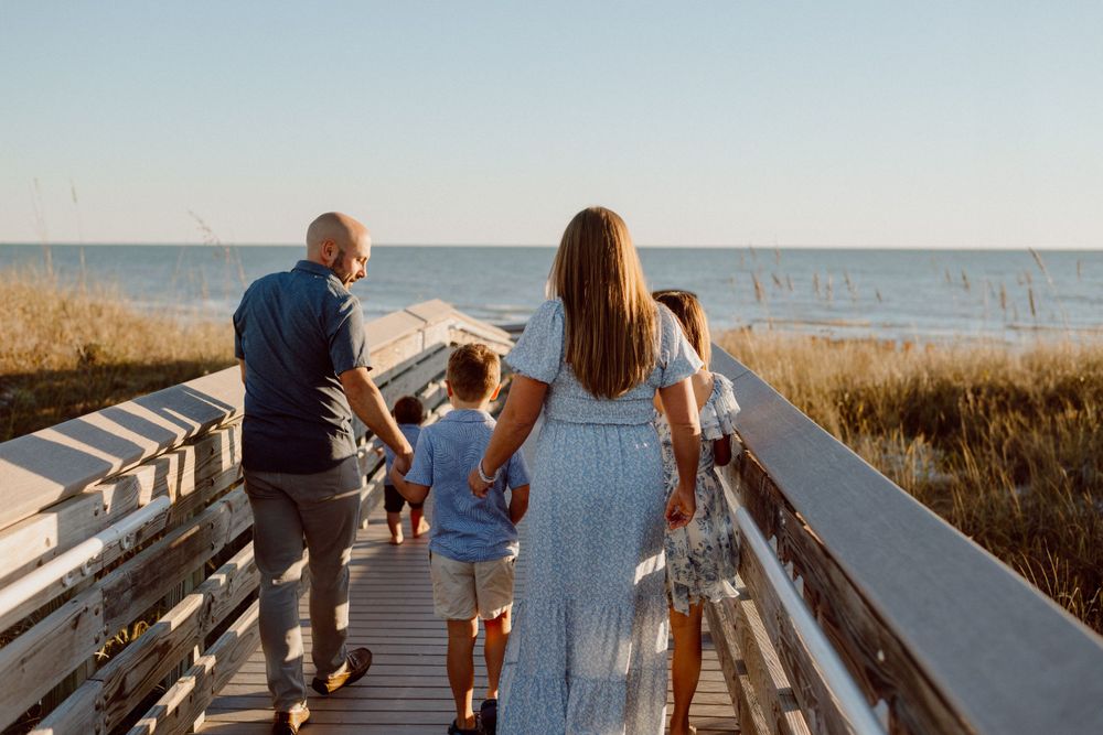 A family walks together on a wooden boardwalk overlooking the ocean.