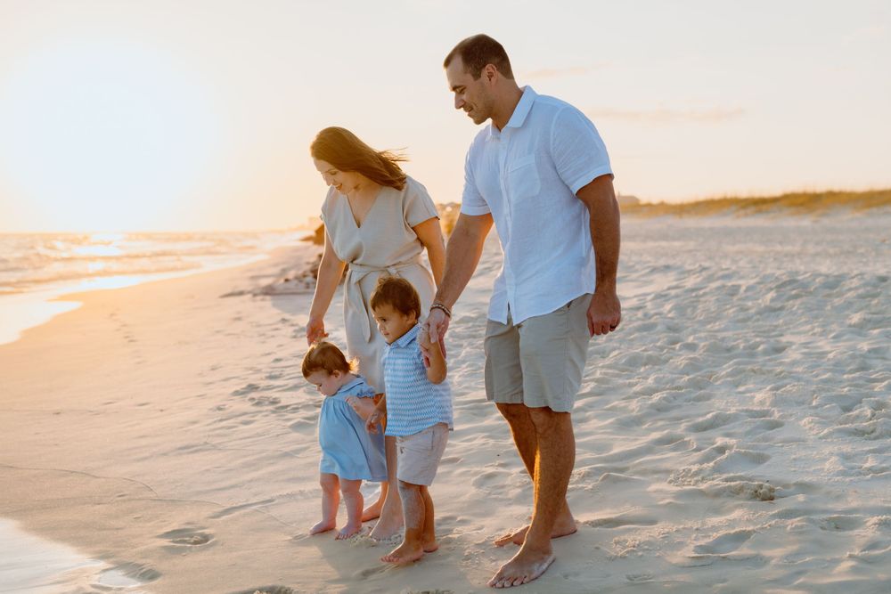 A family walking together on beach at sunset holding hands with small children.