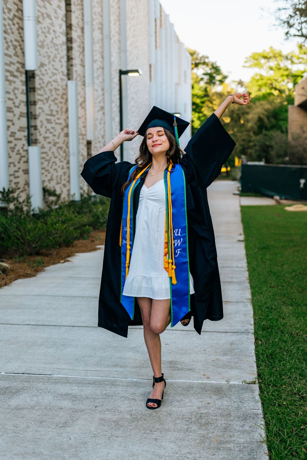 Graduate in academic regalia celebrating on campus walkway.
