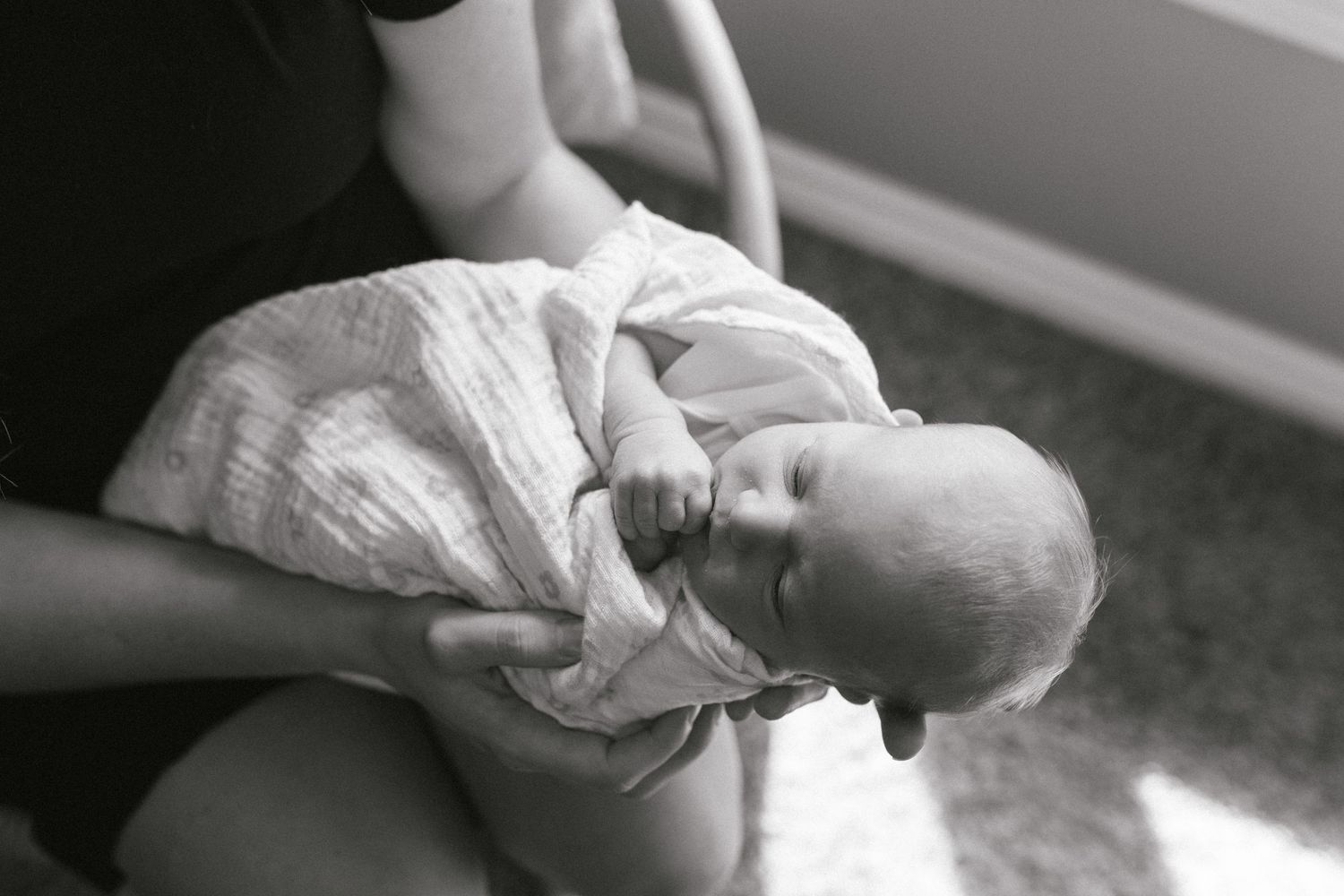 Black and white portrait of tender newborn care by a window.