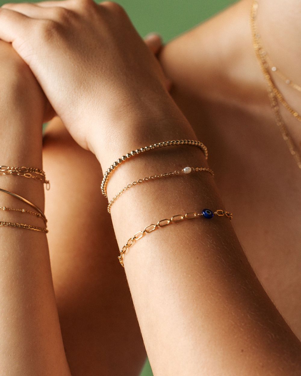 Gold jewelry chains and bracelets delicately arranged in a row on a neutral background.