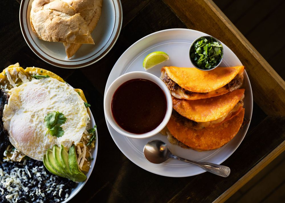 Overhead view of Colombian breakfast with arepas, black bean egg dish with avocado, and a cup of coffee on wooden table.