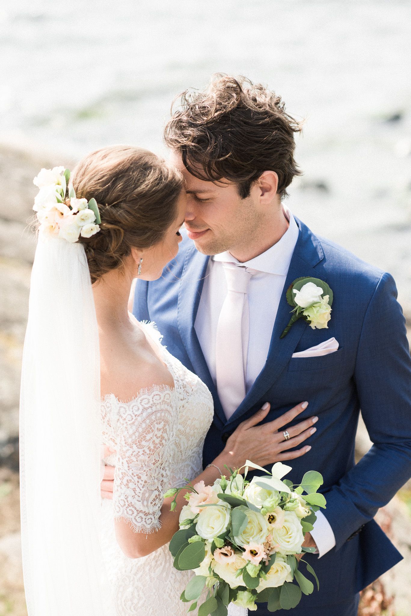 Wedding couple in romantic pose, bride in lace dress with bouquet and groom in navy suit with boutonniere.