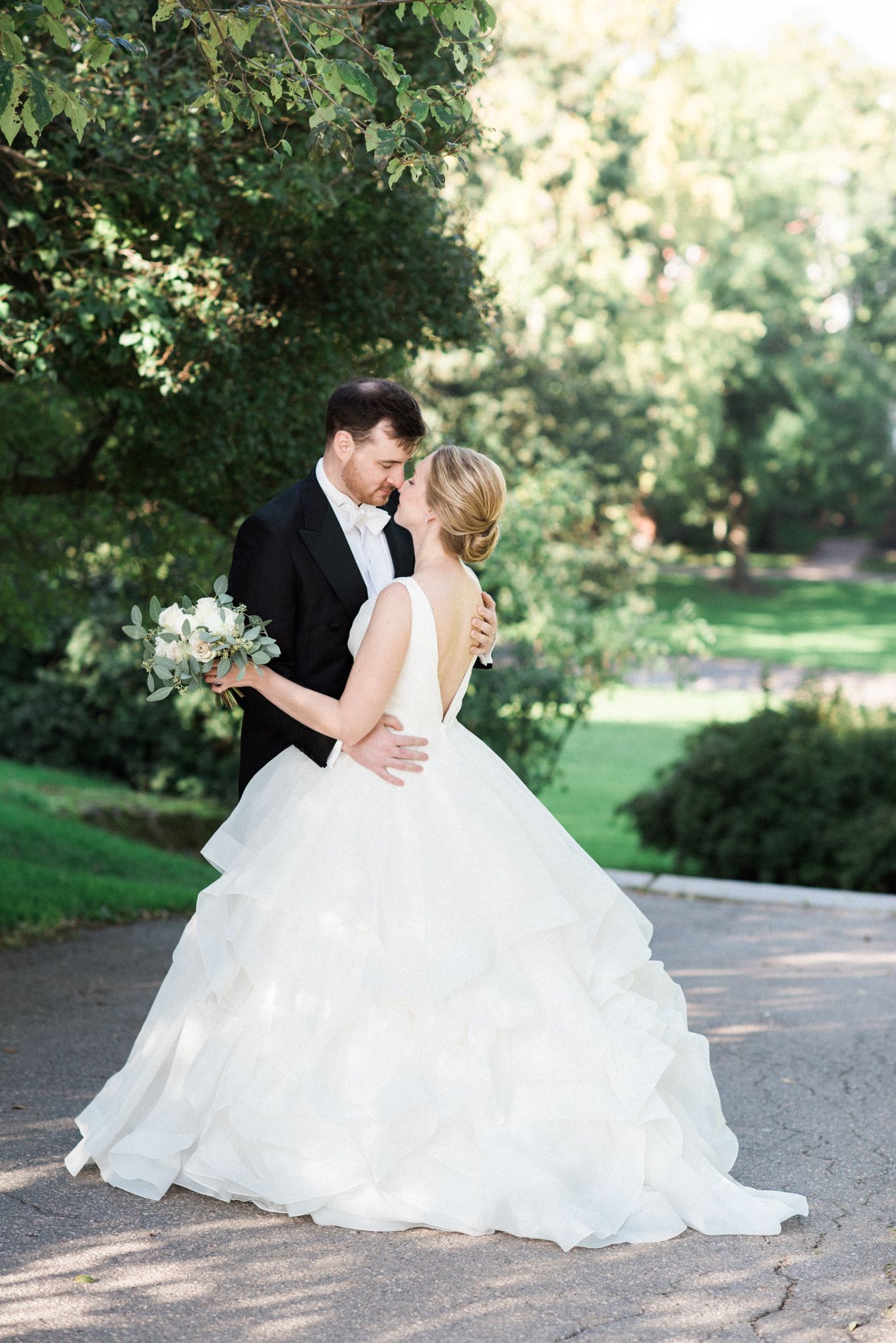 A couple in formal wedding attire share a romantic moment on a garden path surrounded by lush greenery.