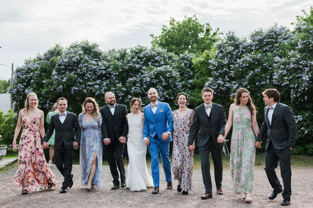 A group in formal attire stands together on a path with blooming trees in the background.