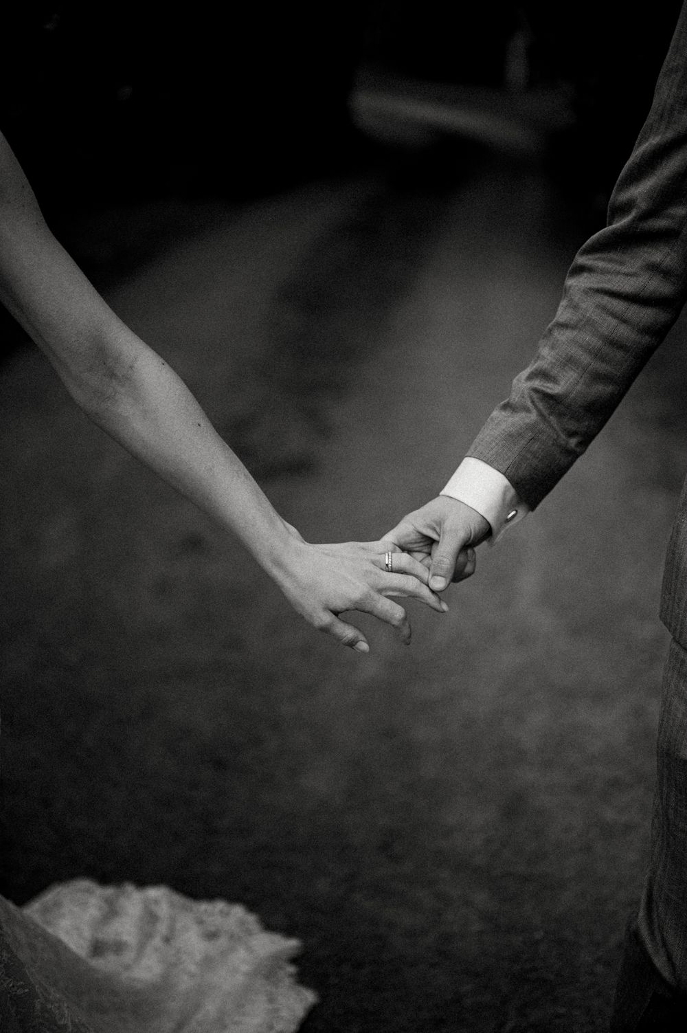 A black and white close-up photo of two hands tenderly holding each other against a dark background.