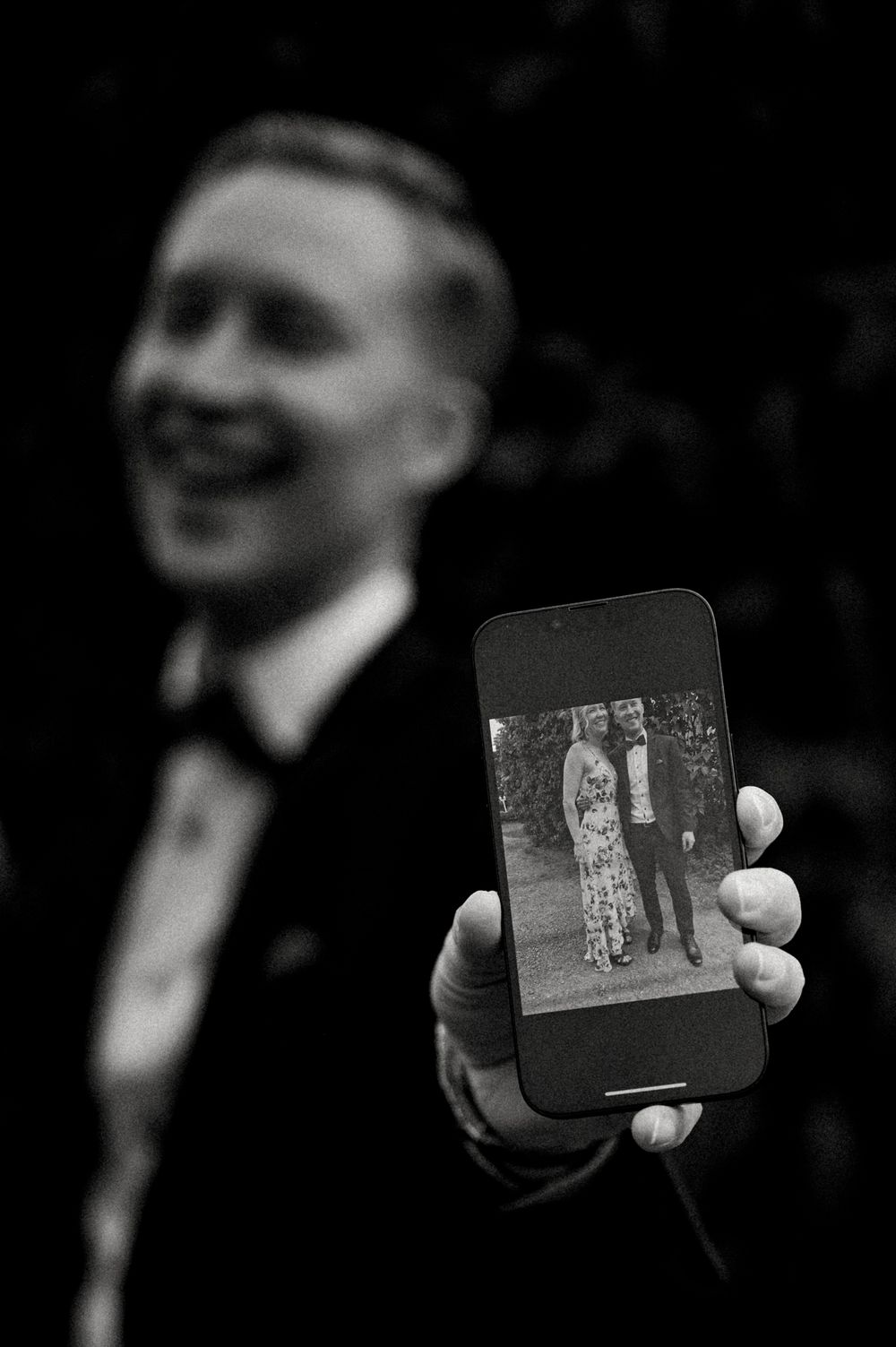 A black and white photo shows someone holding up a phone displaying a vintage photograph.