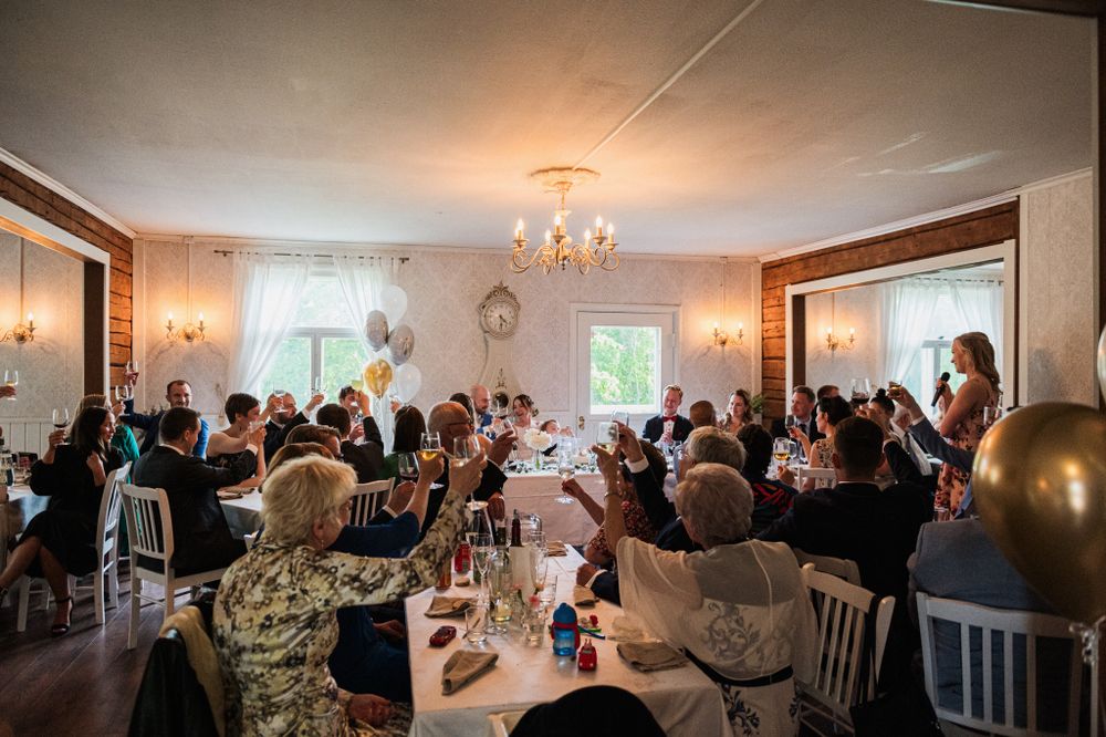 A crowded indoor celebration in an elegant reception hall with chandelier lighting and decorated tables.