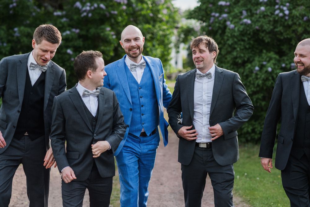A group of men in formal attire laugh together while walking outdoors during a wedding celebration.