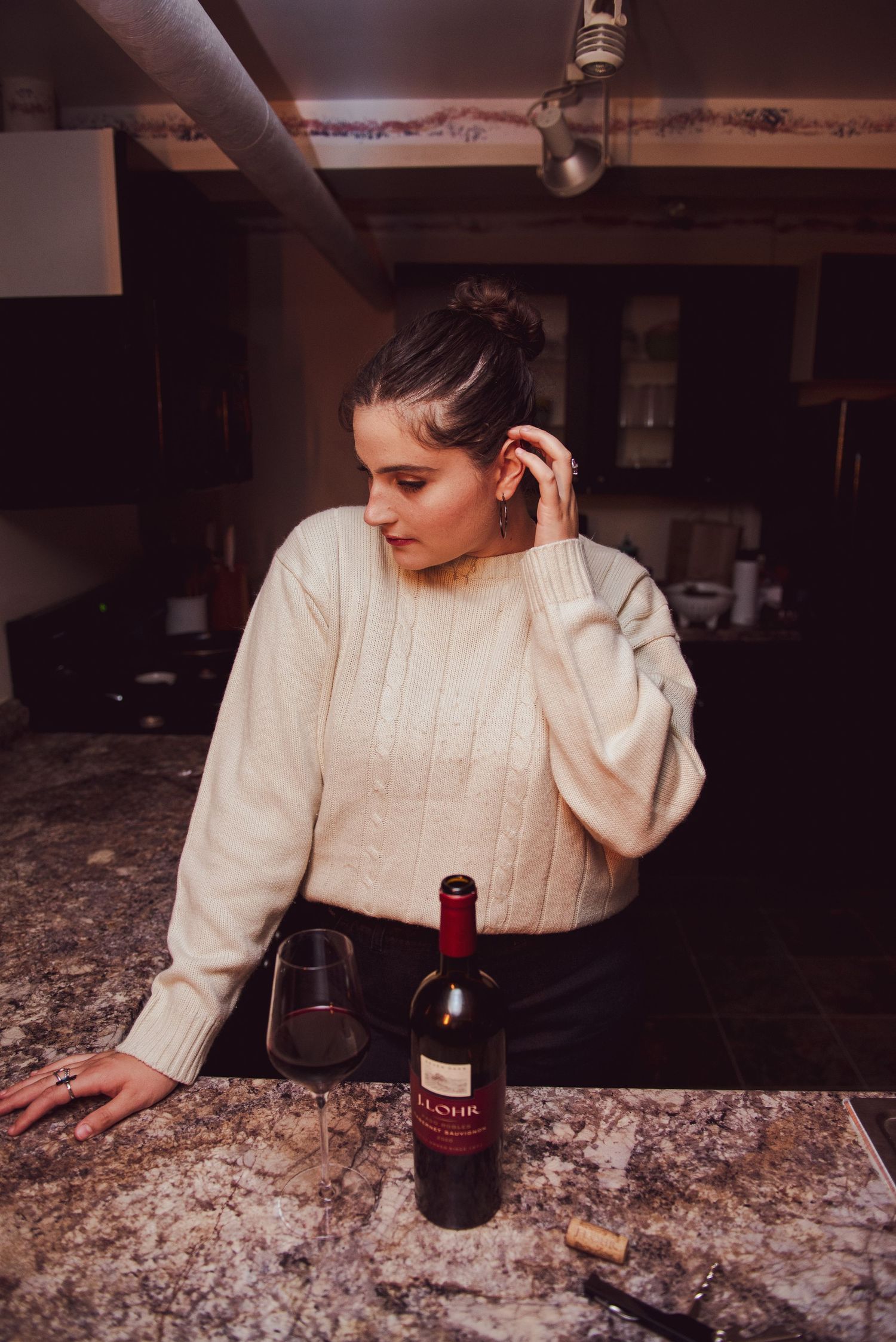 Cozy kitchen scene with cream sweater, wine bottle and moody lighting.