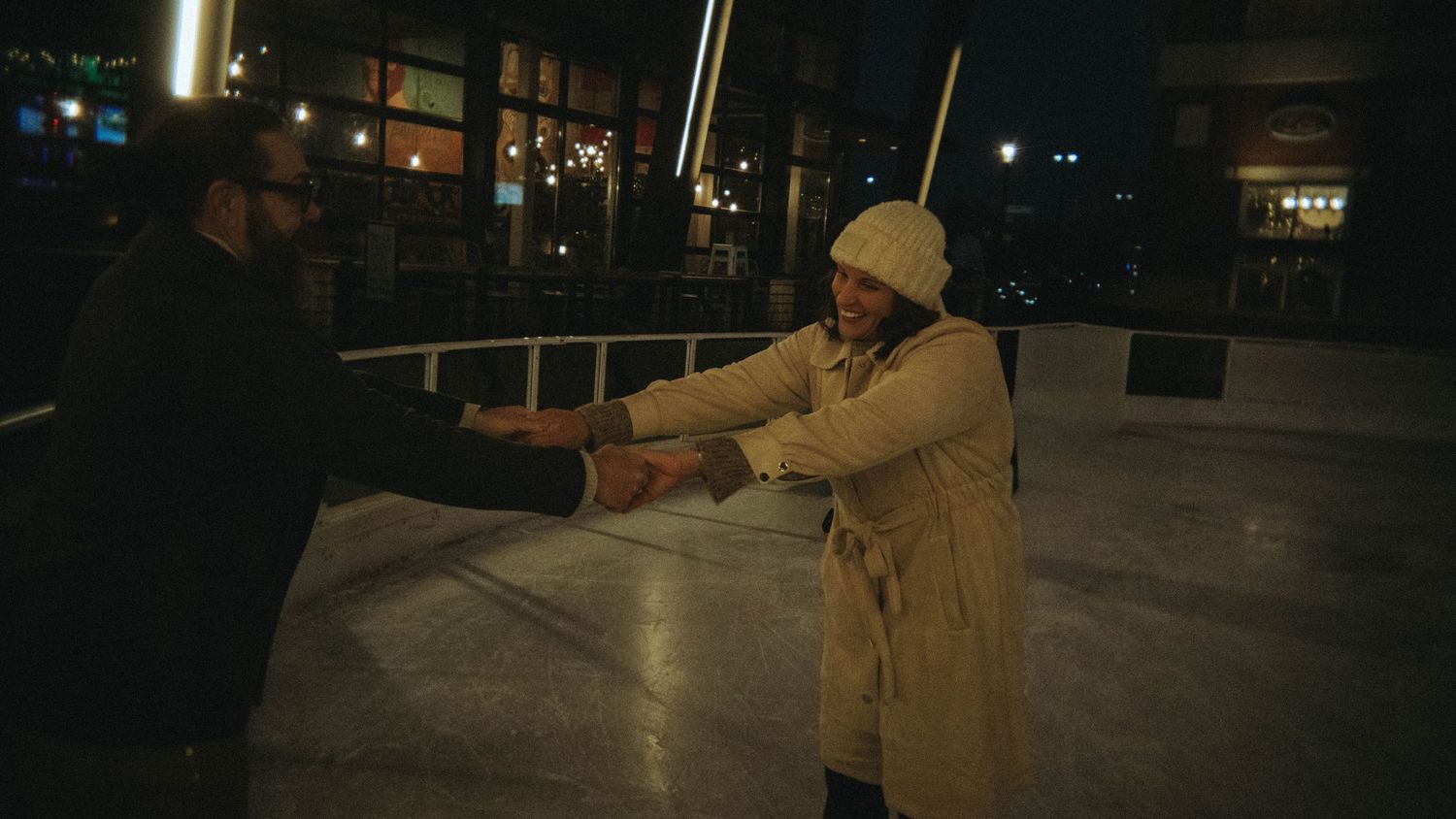 Couple holding hands and playfully pulling each other while ice skating