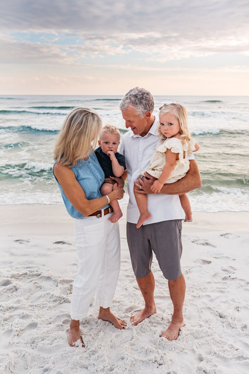 Family photographed together on white sandy beach at sunset.