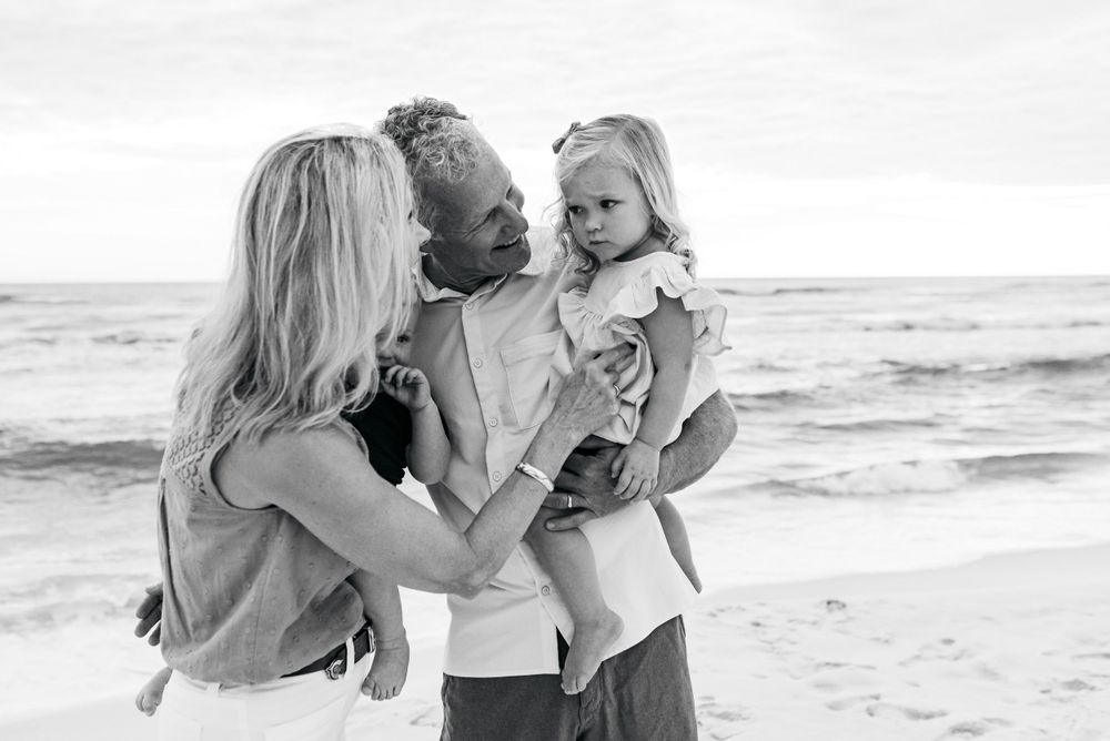 A tender family moment captured in black and white on a beach with waves in the background.
