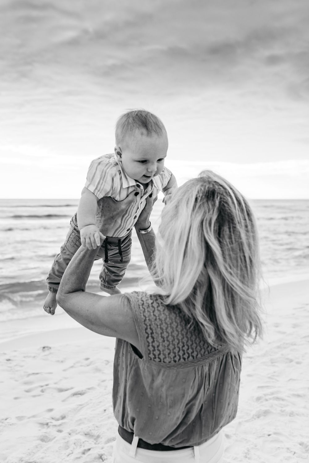 A candid black and white photo of a playful moment between parent and child on a sandy beach.