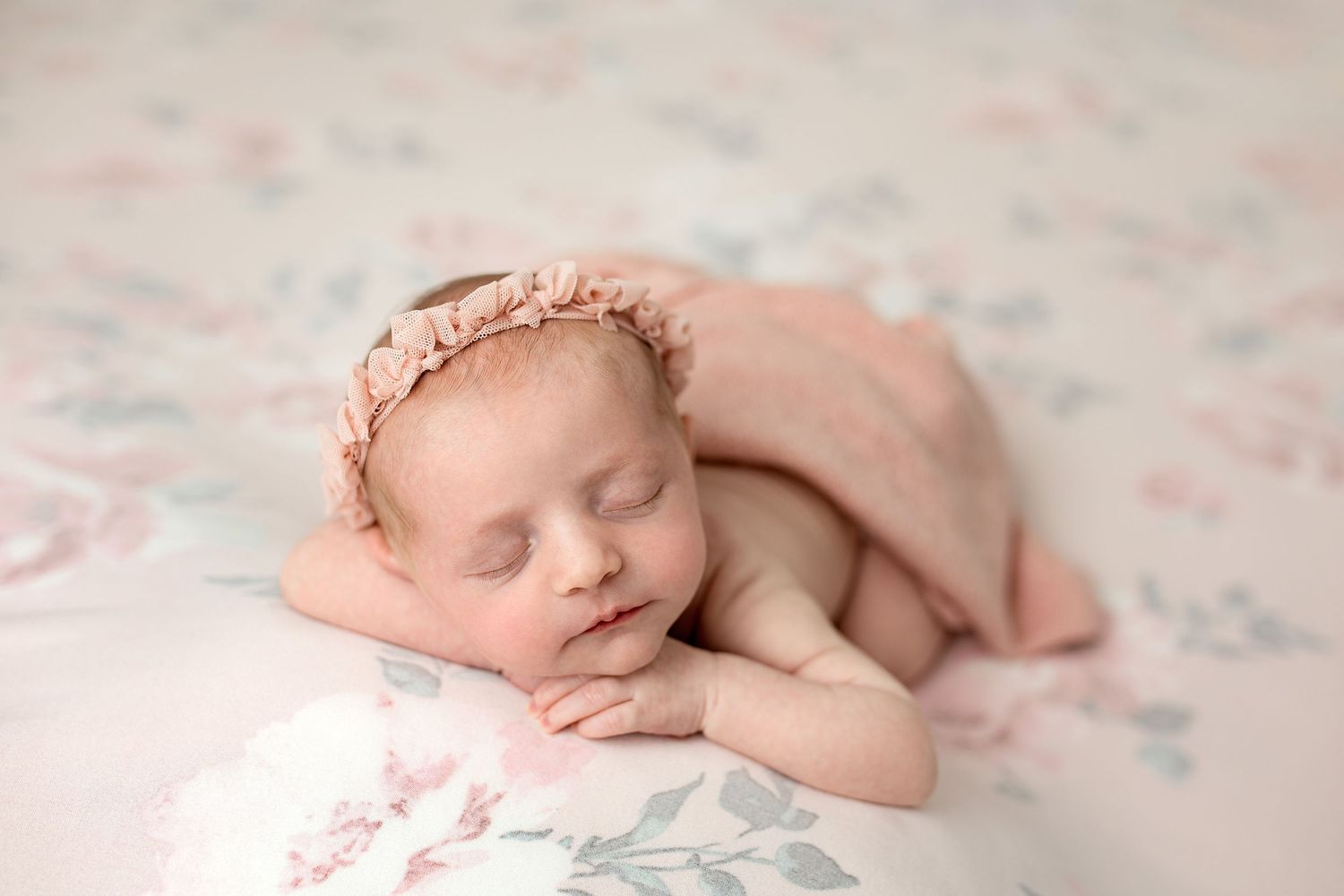 Sleeping newborn wrapped in white swaddle blanket lies in dark bowl on wooden surface.