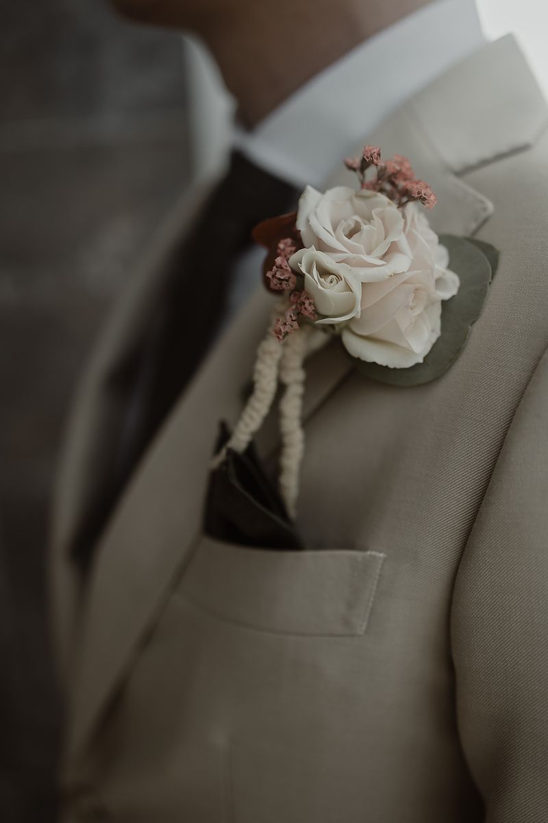 A series of close-up shots showing a delicate white rose boutonniere with pink accents pinned to a beige suit lapel.