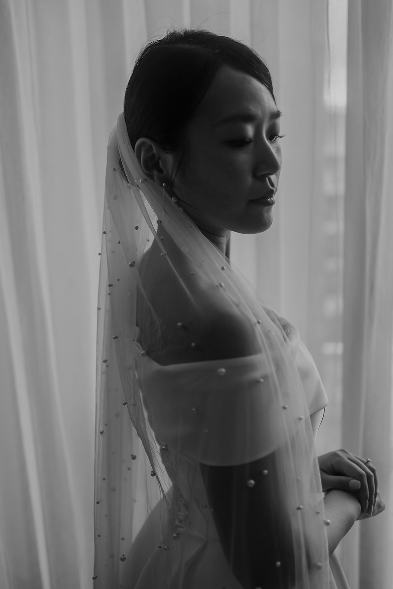 Elegant black and white wedding portrait series showing a bride in delicate veil against soft window light.