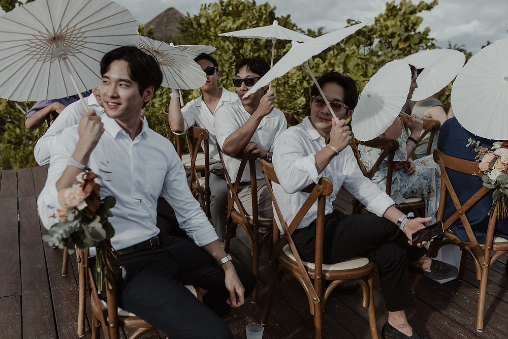 Guests in white holding parasols during outdoor ceremony, destination wedding Trs coral costa mujeres.