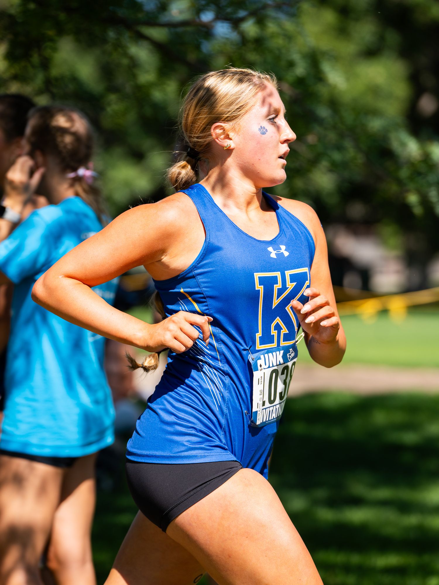 Runner in blue Under Armour tank top competing in outdoor cross country race on sunny day.