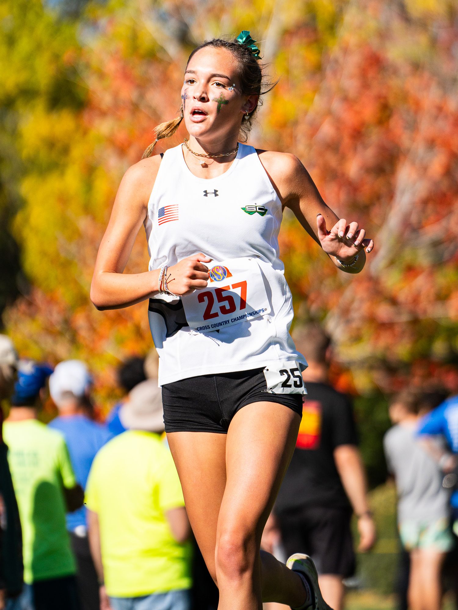 Cross country runner competing in a fall race wearing white uniform with vibrant autumn foliage in background.
