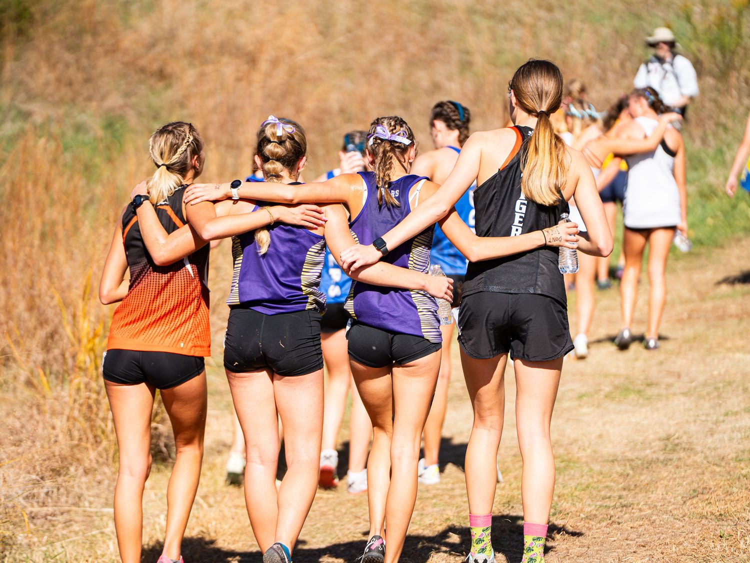 Group of runners walking together on a trail wearing athletic gear during cross country practice.