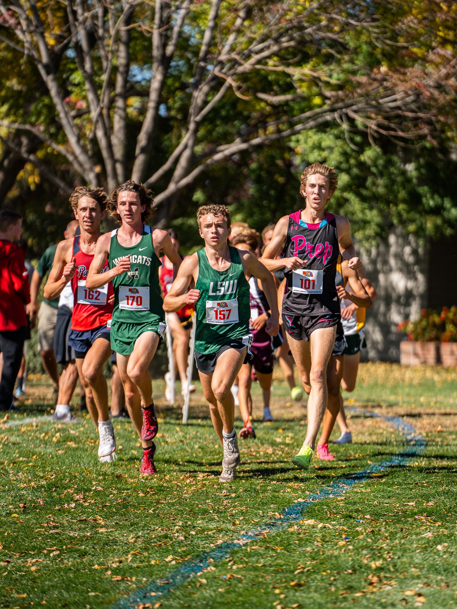 Pack of cross country runners competing on grassy course during fall meet.