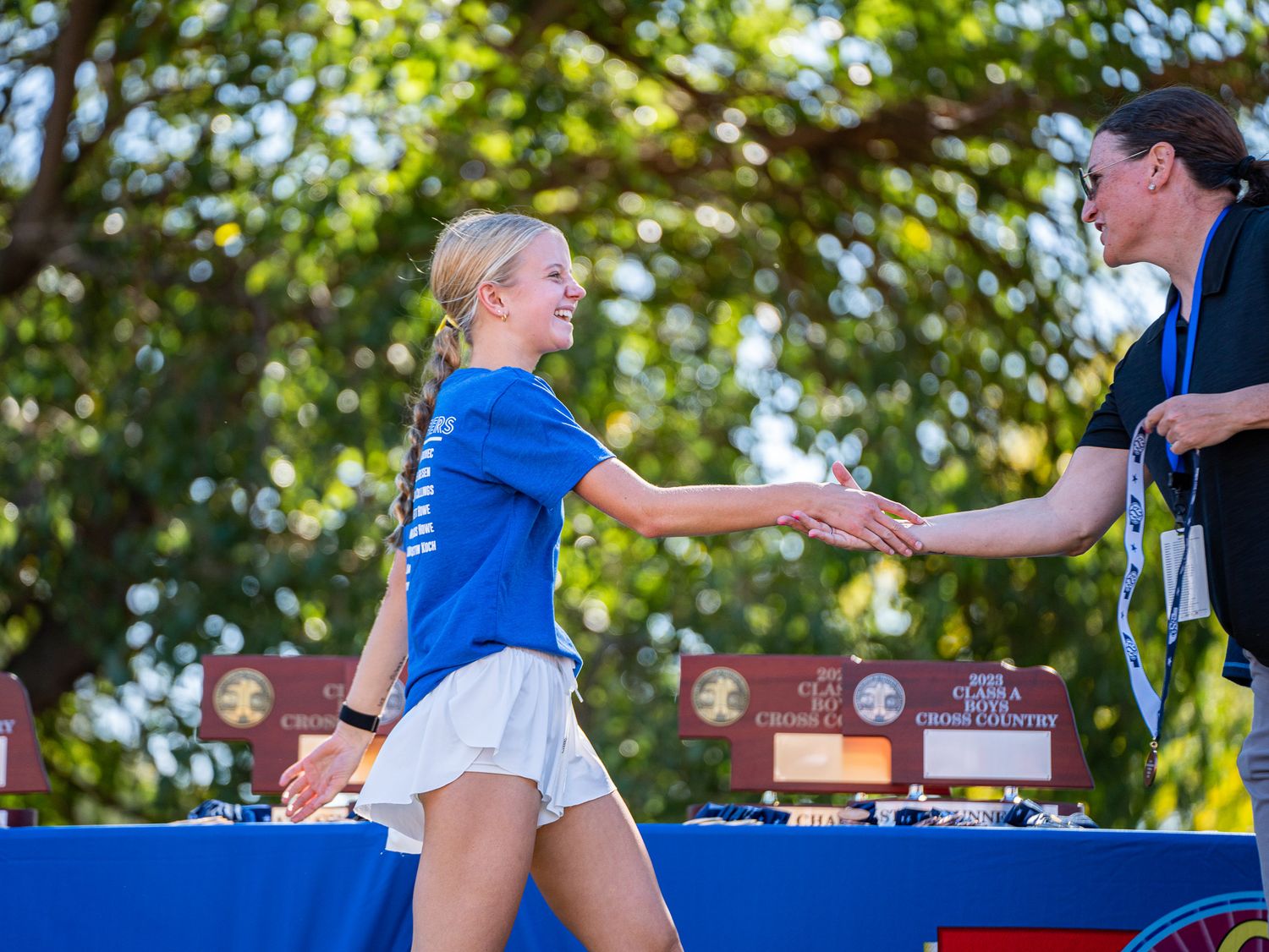 Athlete receiving award at cross country meet awards ceremony with judges table in background.