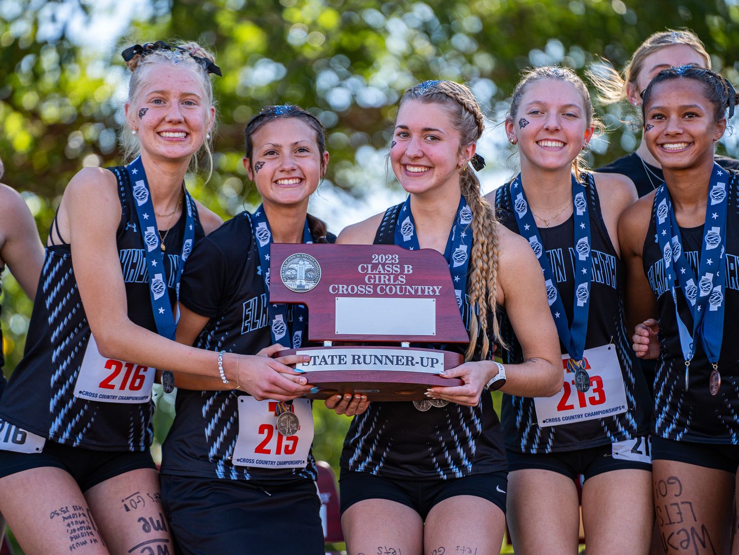Cross country team members celebrate with championship plaque after winning competition.