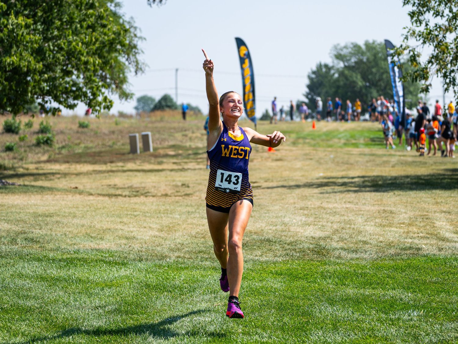 Runner celebrates with arms raised while crossing finish line on sunny race course.