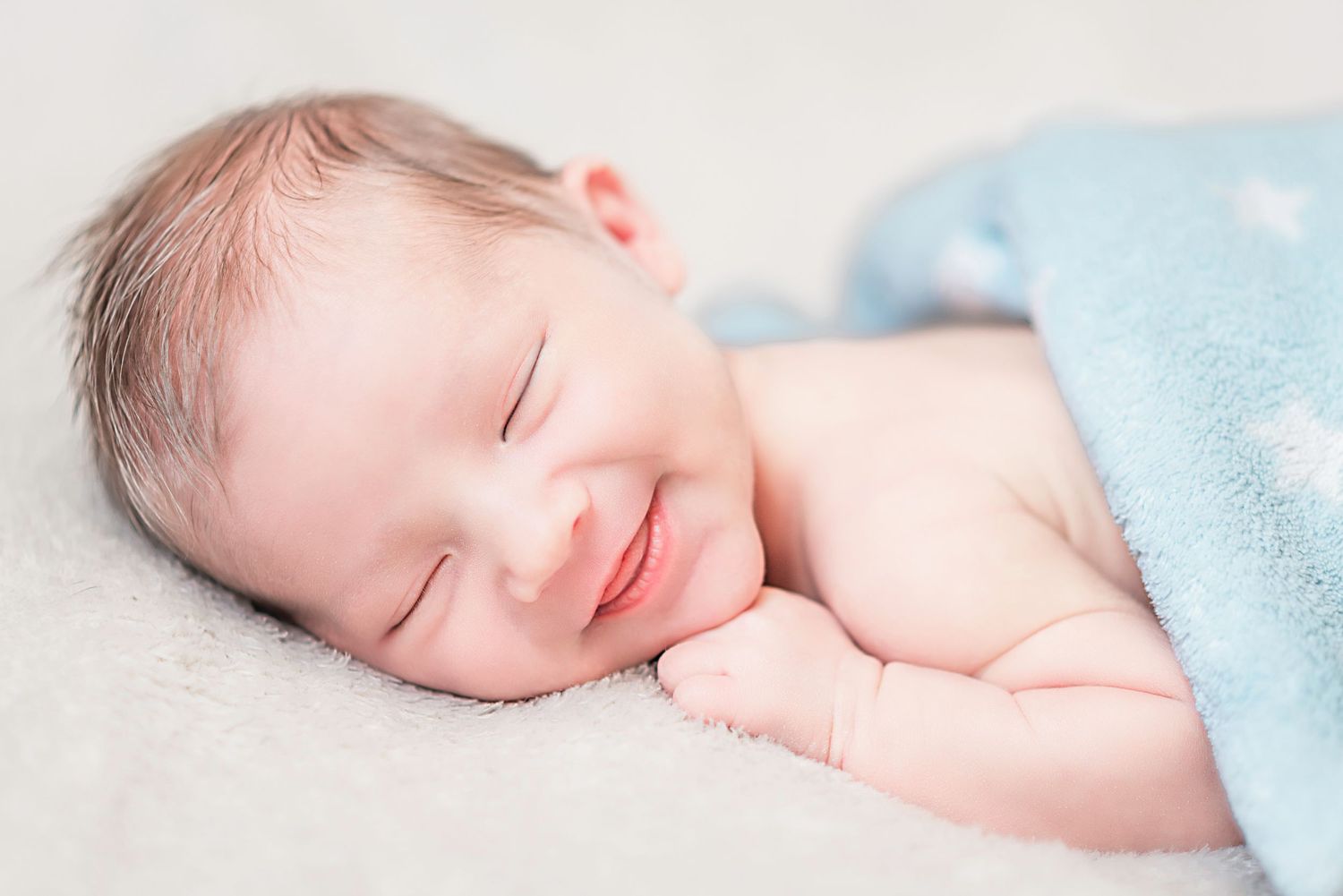 A peaceful sleeping newborn baby with a slight smile lies under a soft blue blanket. újszülött fotózás, newborn photography, lovely details