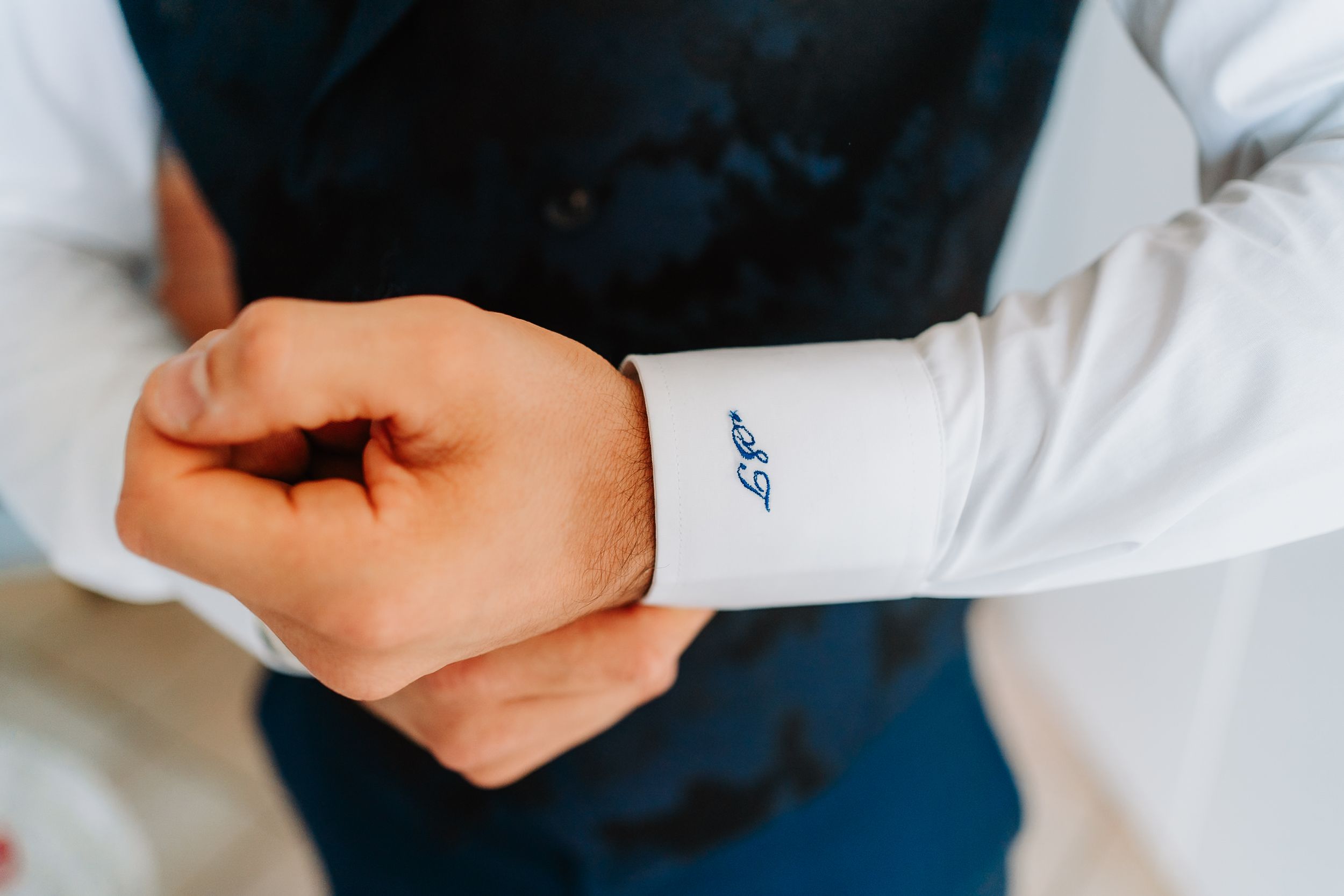 A person wearing a white dress shirt with a small blue logo pulls back their sleeve cuff.