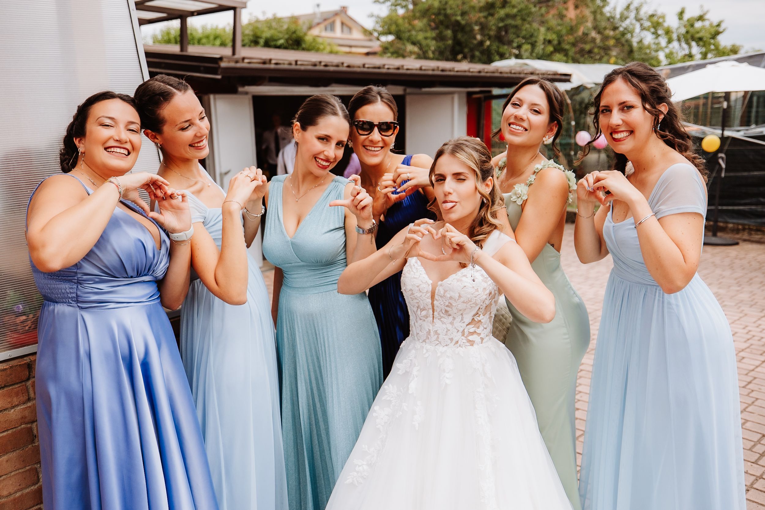 A bridal party wearing pastel blue and mint bridesmaid dresses shares a joyful candid moment together outdoors.