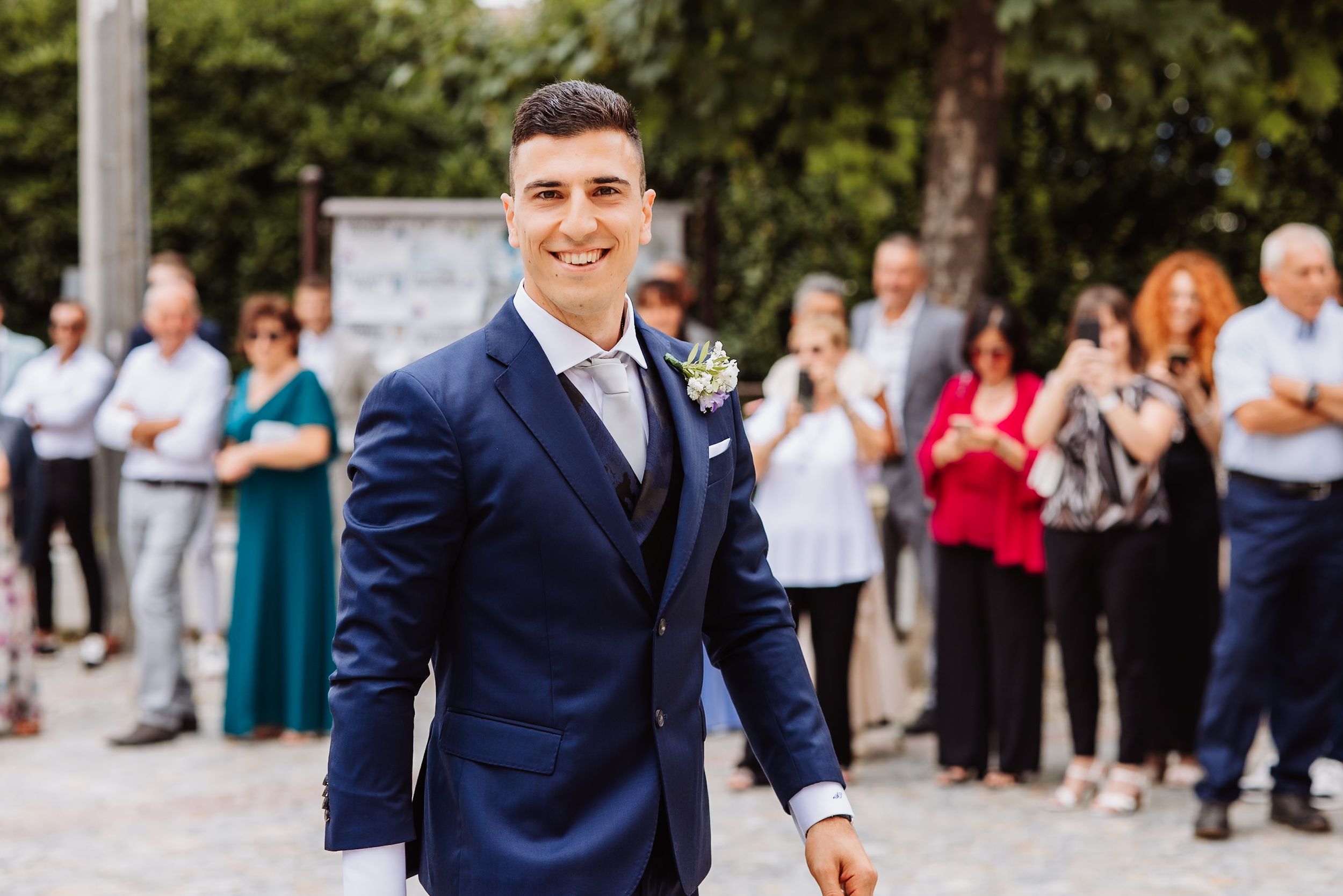 Couple in navy blue wedding attire celebrates joyfully with guests outdoors on their special day.