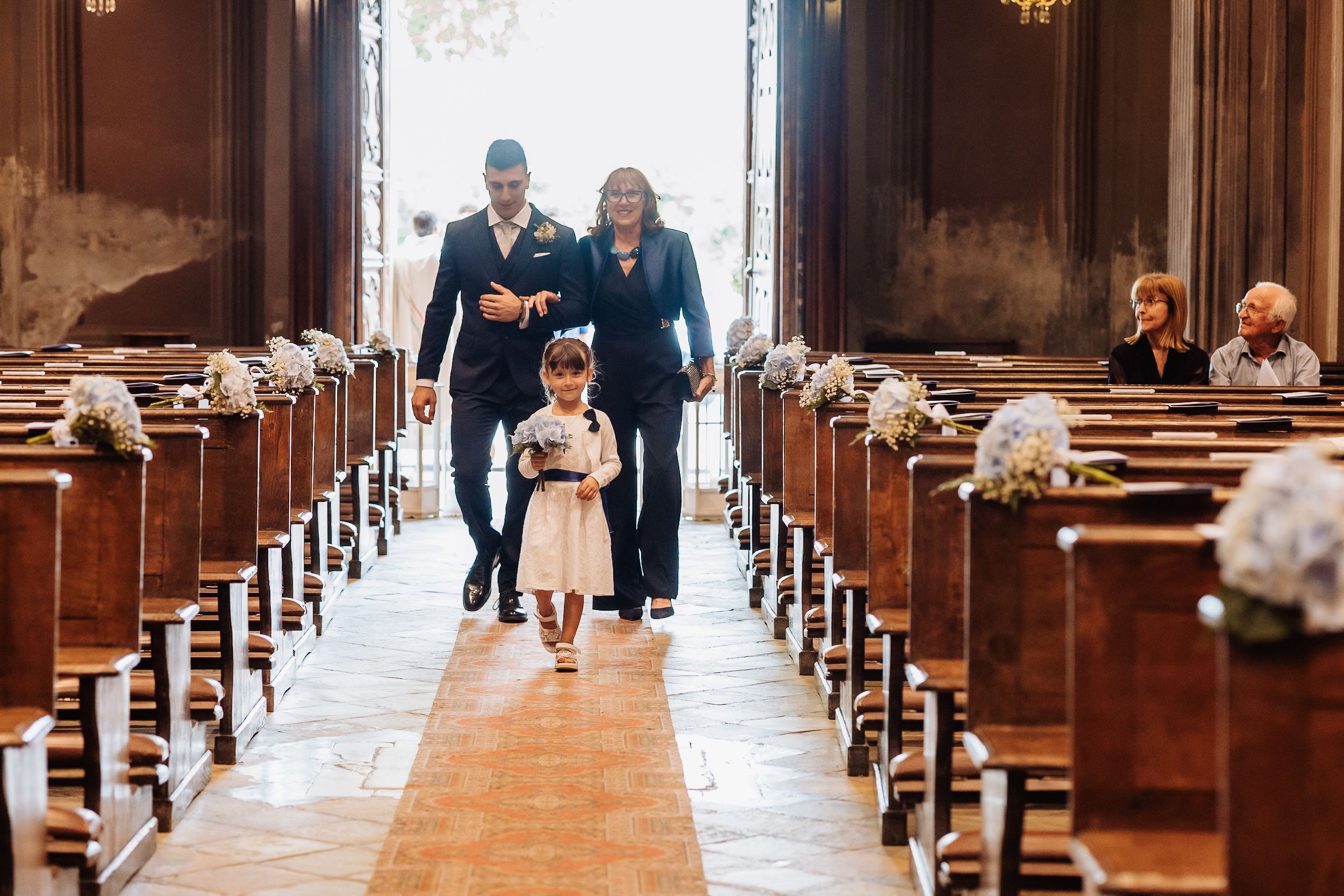 People walking through the grand aisles of a traditional wooden church interior illuminated by warm lighting.