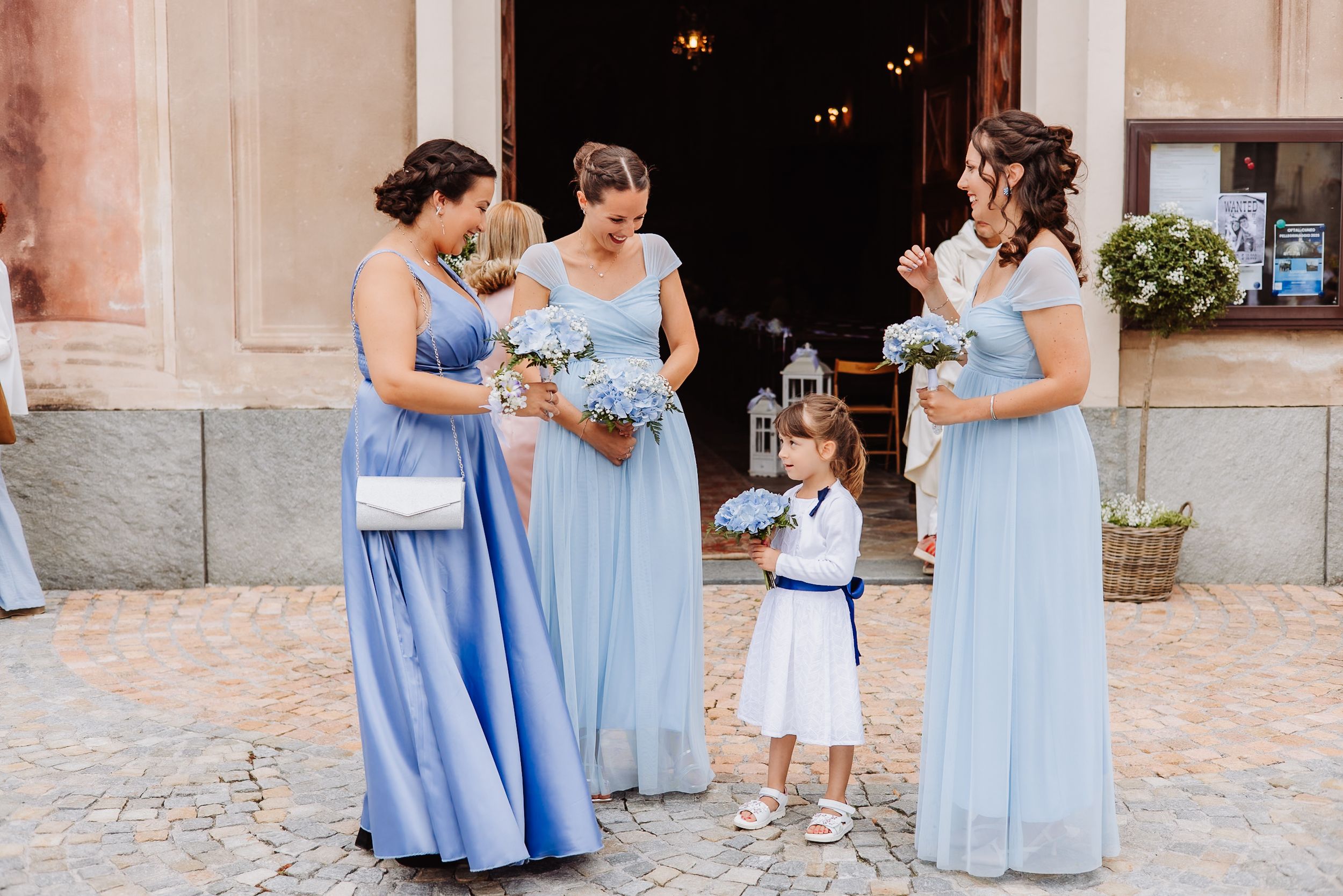 Bridesmaids in flowing light blue dresses stand together in an elegant venue during a special occasion.