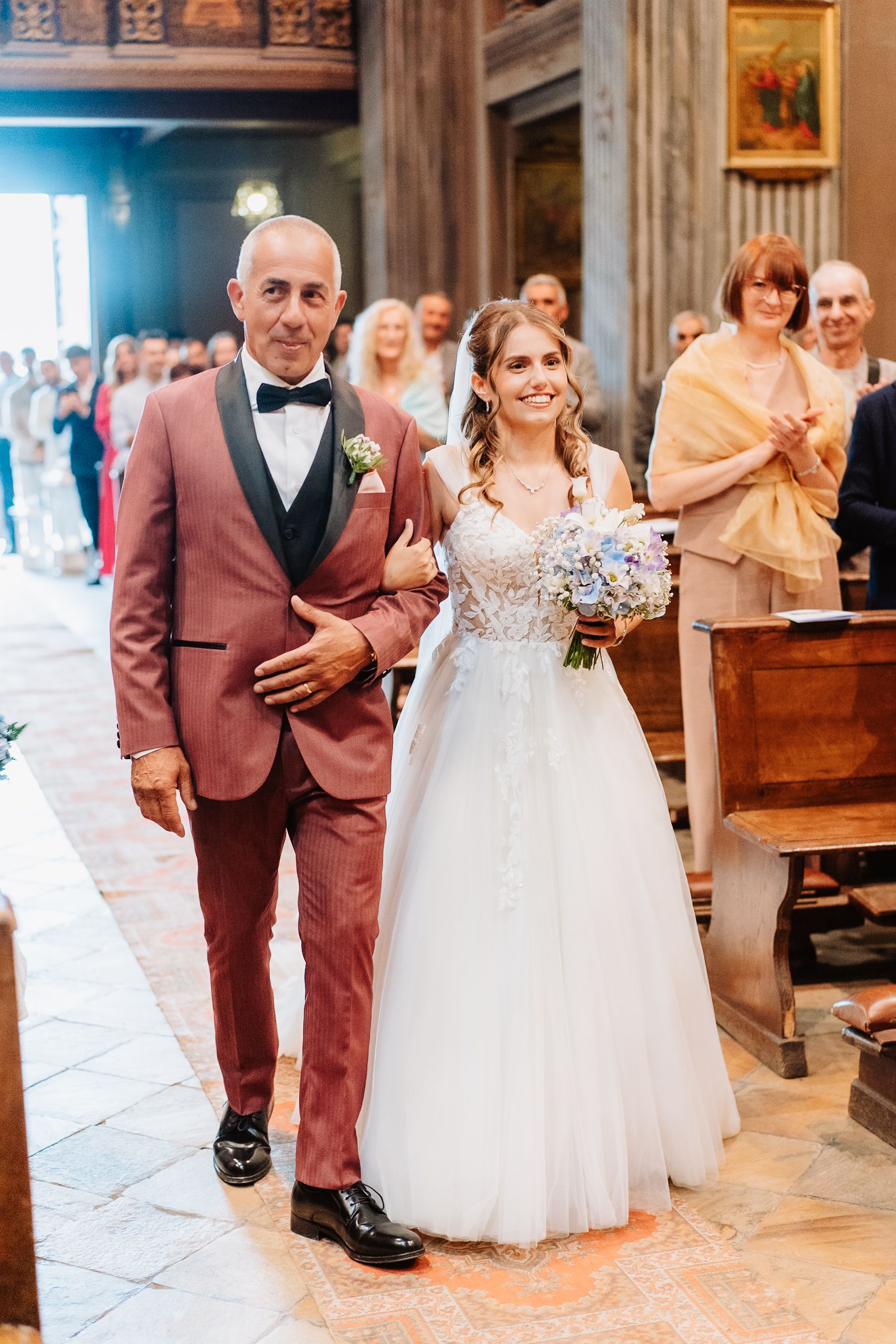 Wedding couple walks down the aisle in a rustic church hall with guests looking on.