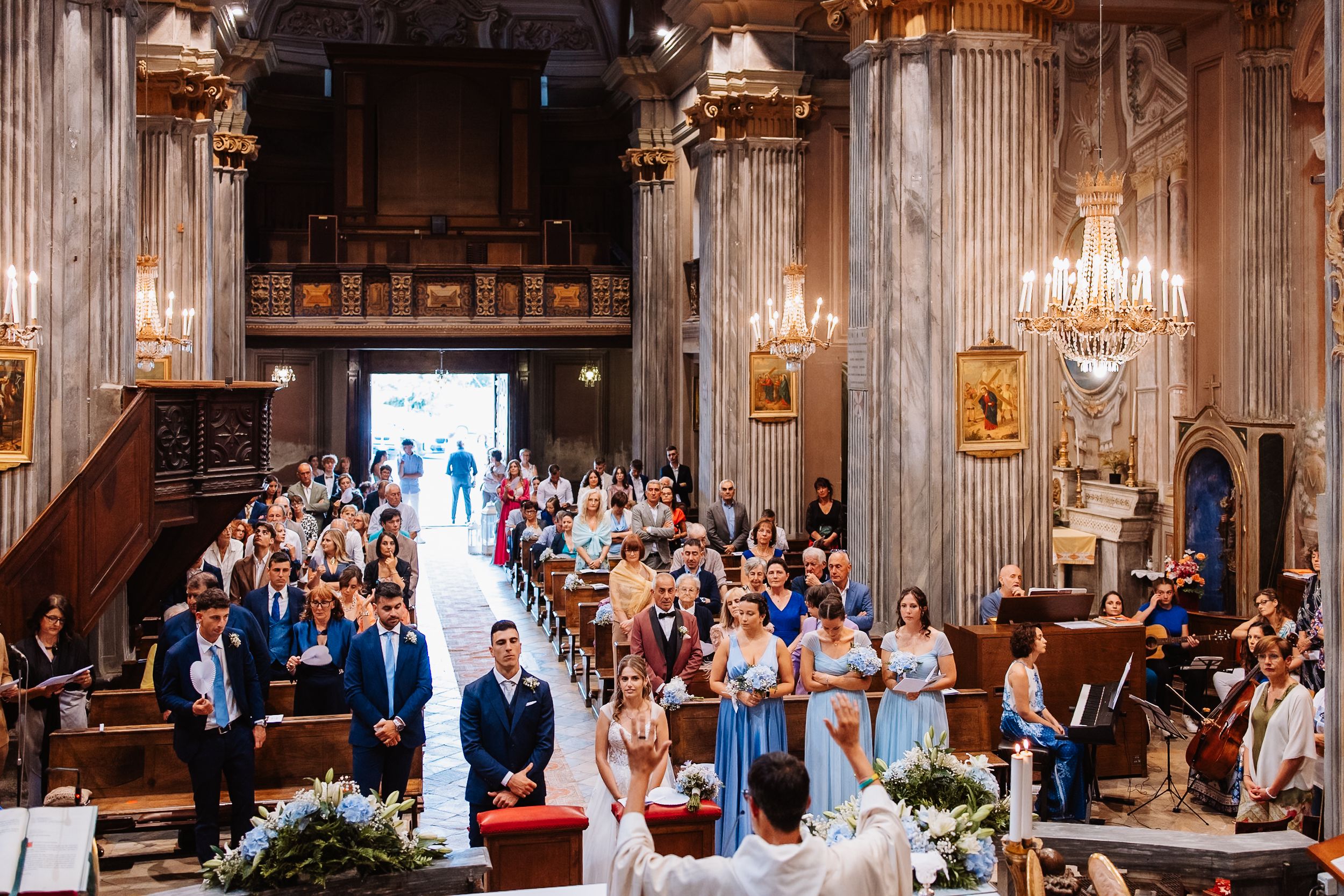 Wedding celebration inside a grand historic cathedral with ornate architecture and crystal chandeliers hanging from above.