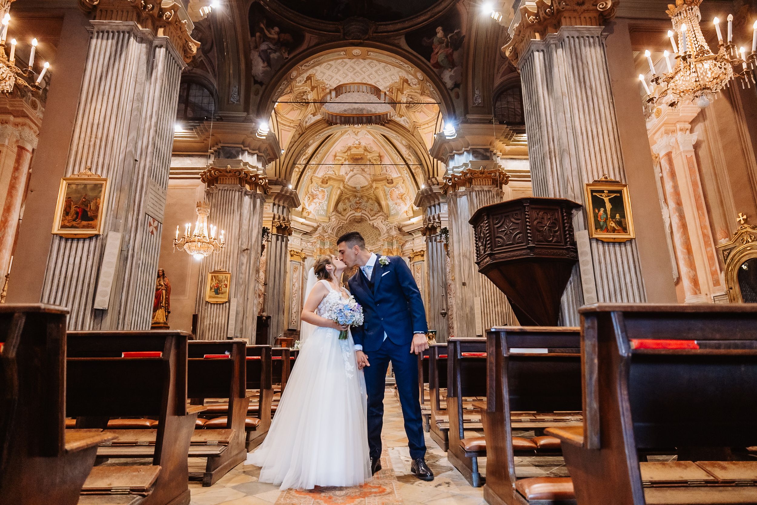 Elegant wedding ceremony taking place in a baroque church with golden details and dramatic lighting.