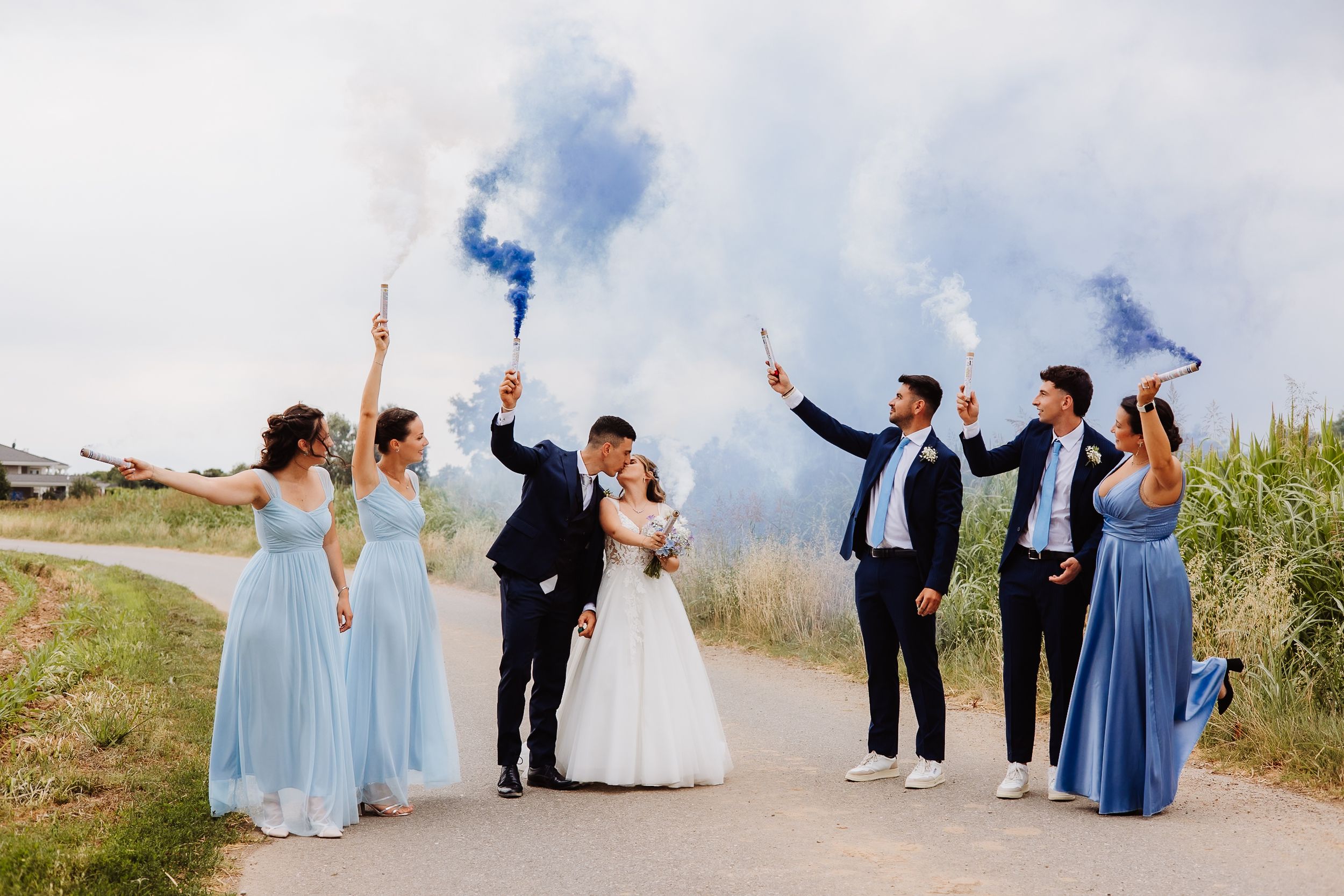 Wedding group poses against scenic coastal backdrop wearing blue and white formal attire.