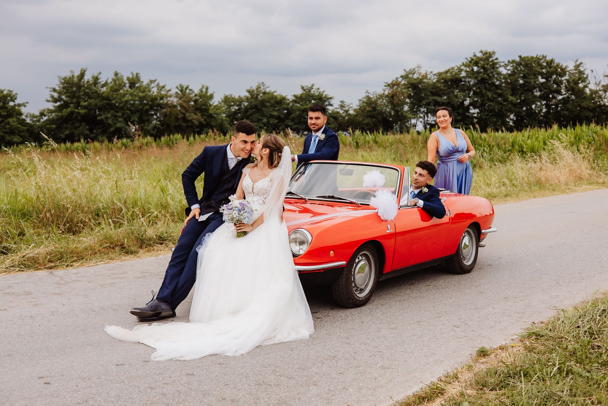 A red vintage convertible car parked on a gravel road during a sunny summer day.