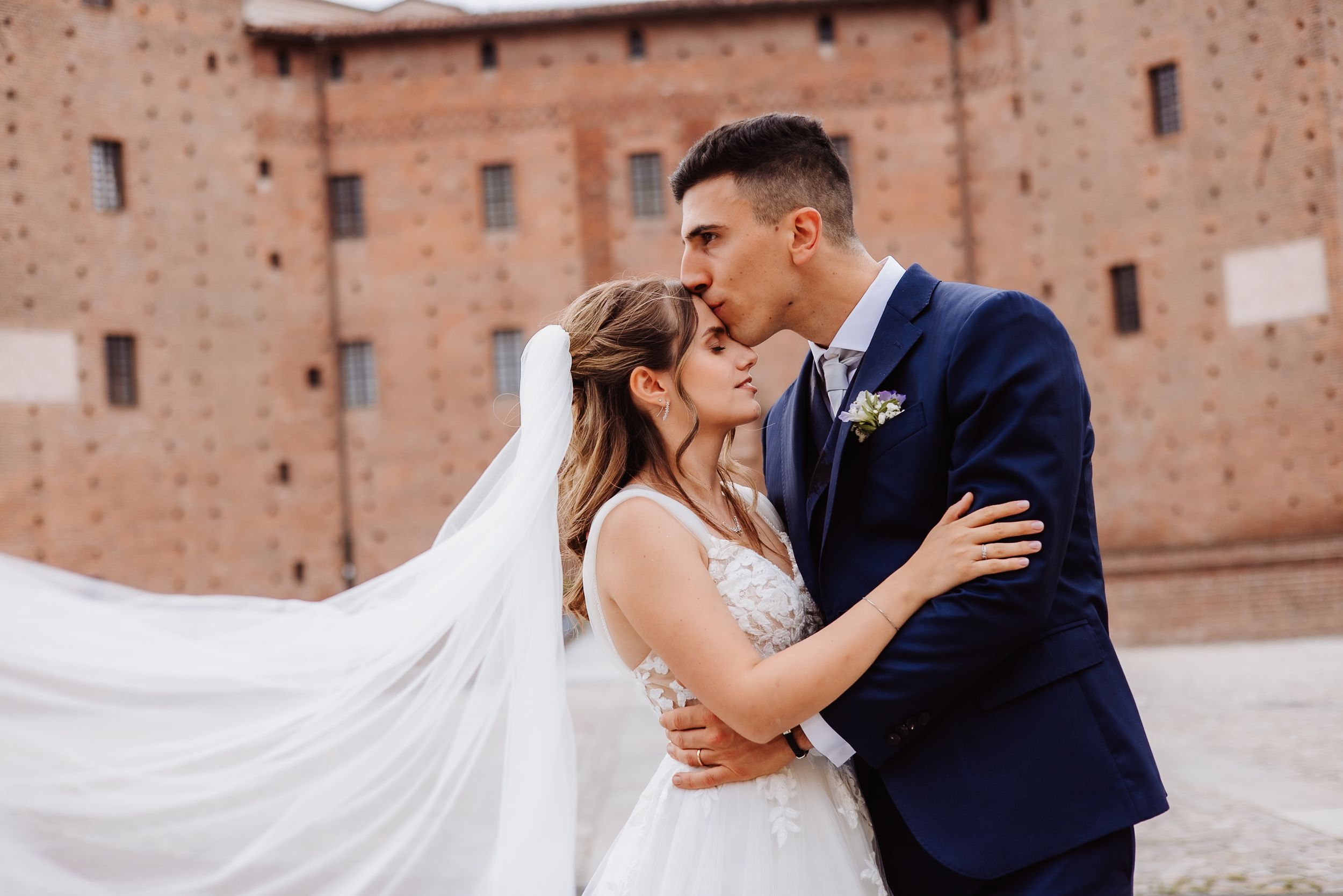 Couple embracing against rustic brick wall backdrop at wedding venue.