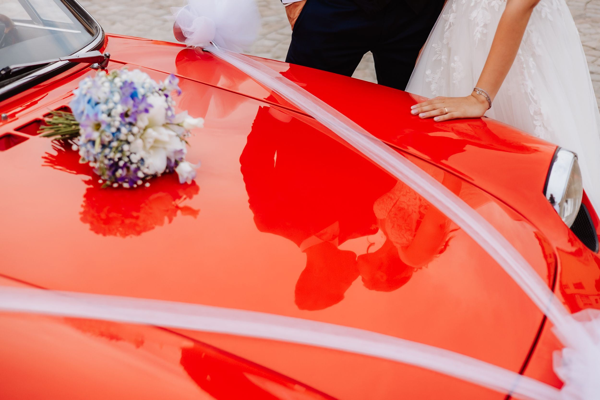 Close-up details of red vintage car hood with wedding bouquet and floral decorations.