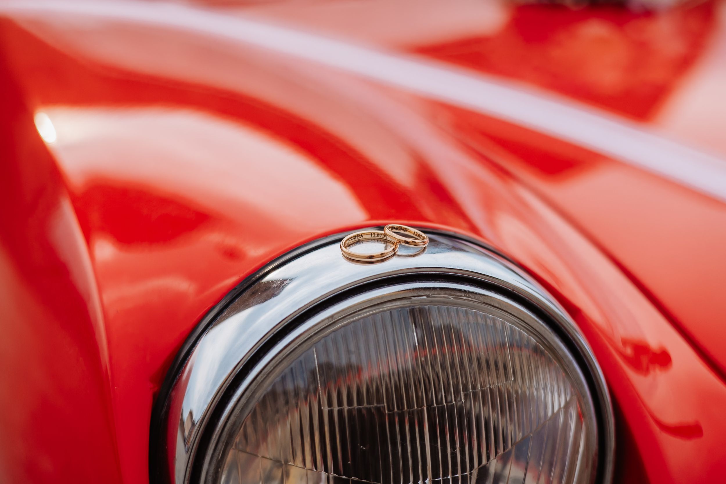 Close-up view of a vintage red Ferrari car with chrome headlights and polished bodywork shining in bright lighting.