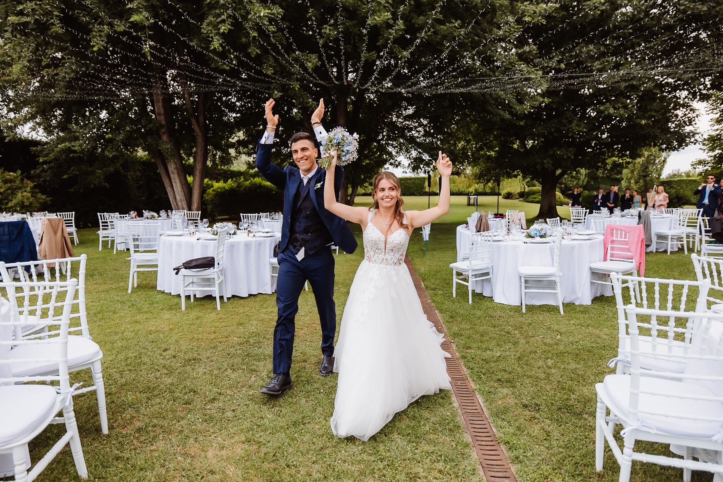 Newlyweds dance together surrounded by white garden chairs set up for an outdoor wedding ceremony.