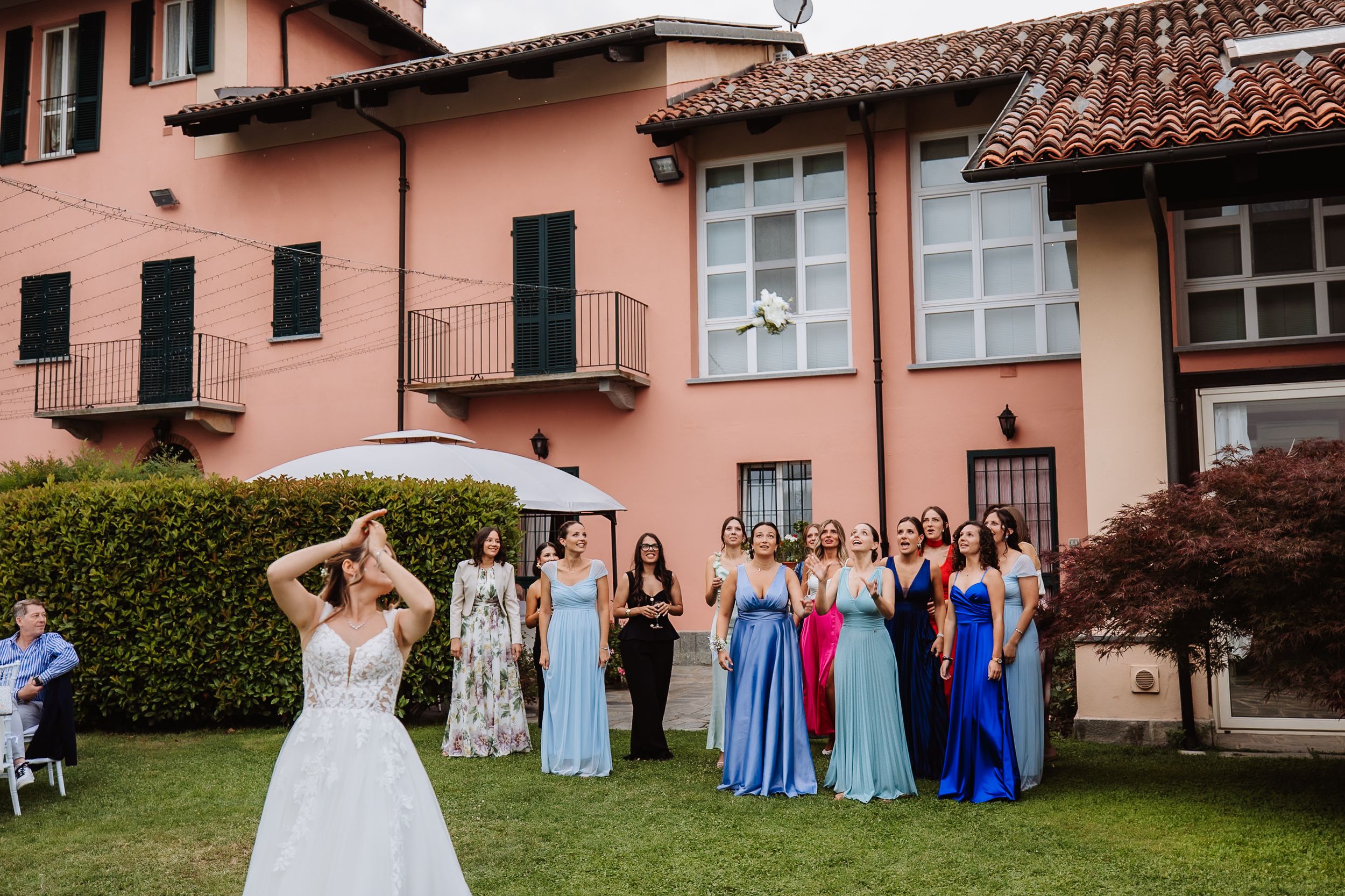 Wedding party poses together in front of a pink stucco building with tiled roof during outdoor celebration.