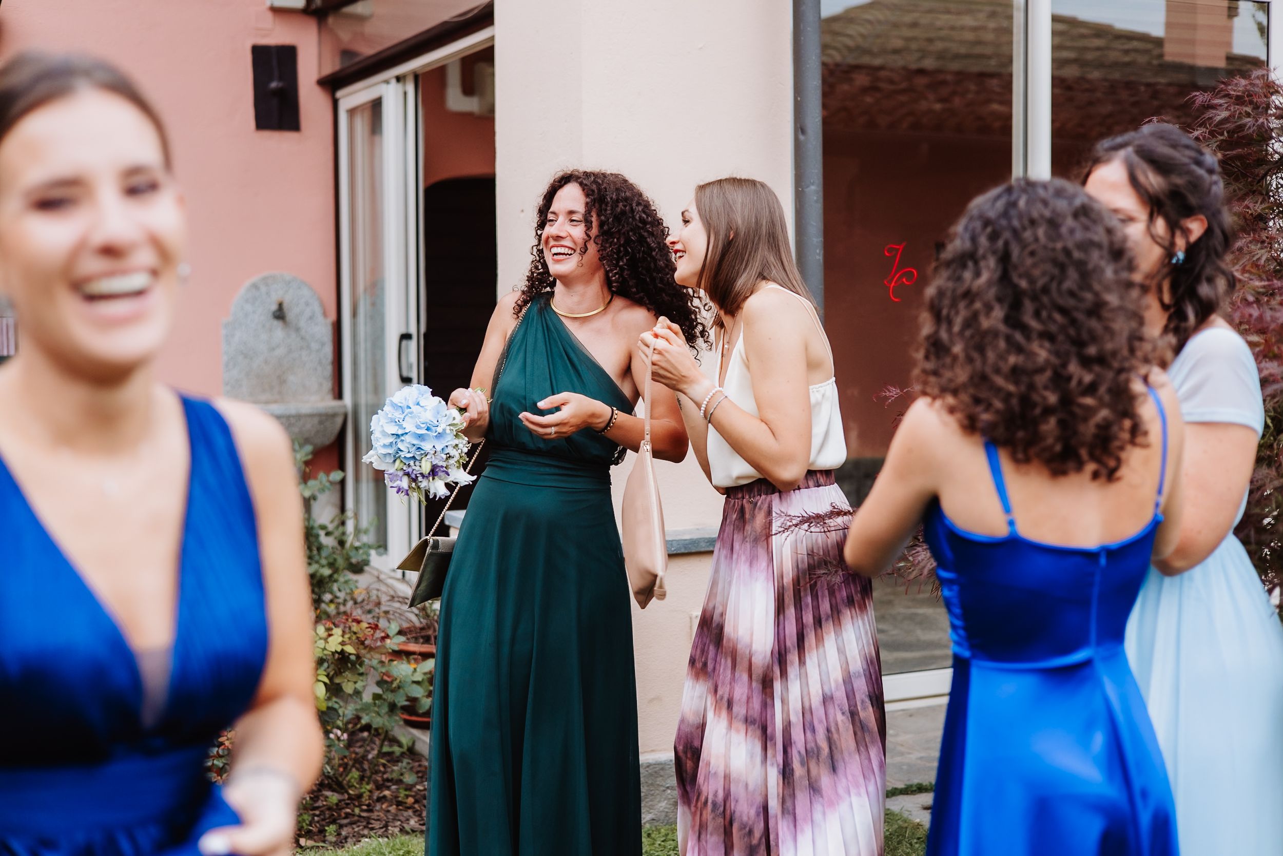 Group of wedding guests wearing bright blue and emerald green dresses dancing and celebrating at an indoor venue.