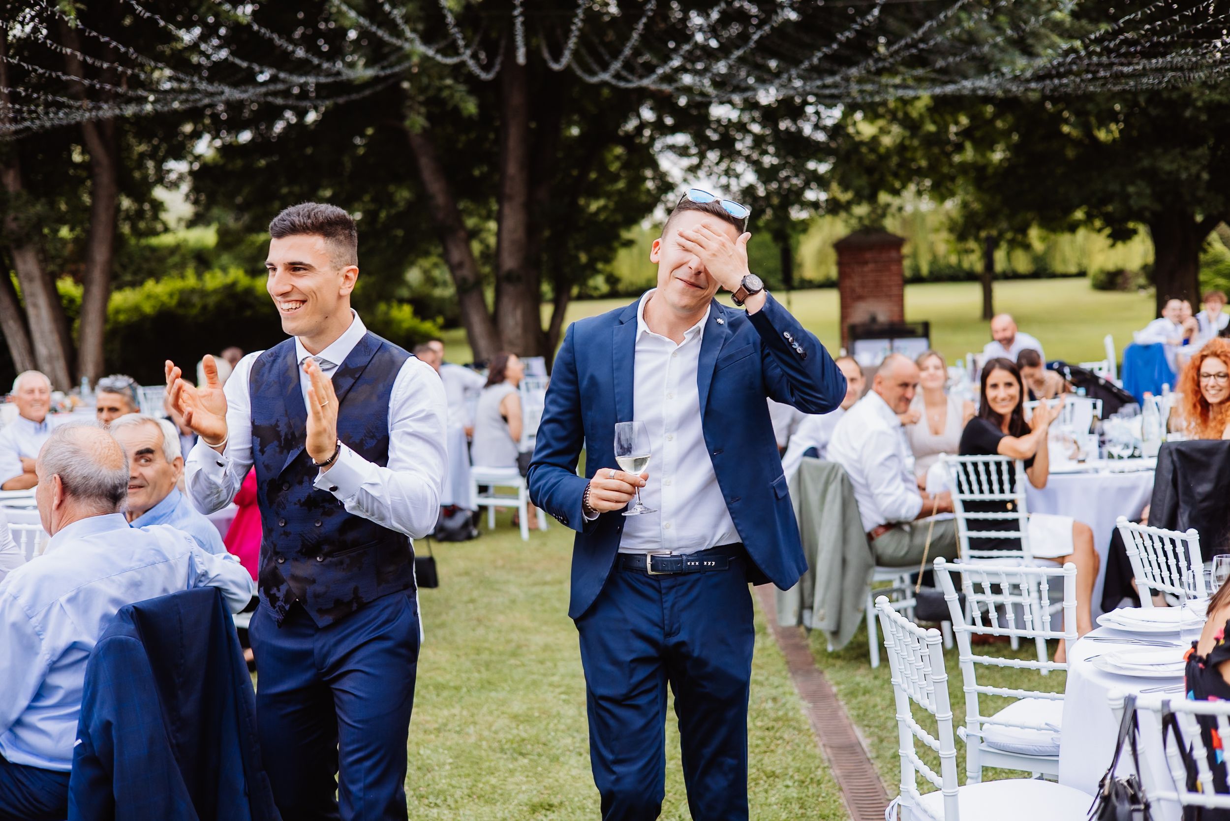 Wedding guests celebrate on an outdoor lawn with white chairs and navy blue attire.